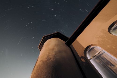 The image showcases a low-angle view of a tower under a starry night sky with star trails creating a dynamic effect.