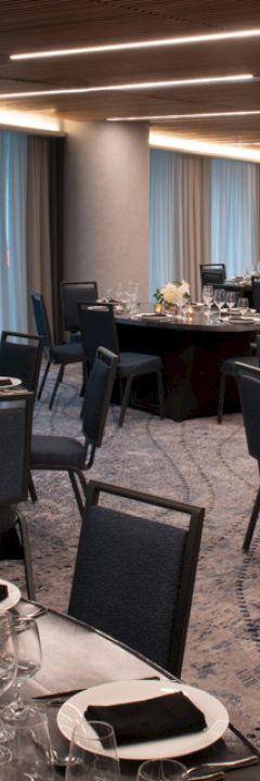The image depicts an elegant dining room with black-topped tables set for a formal event, featuring dark chairs and soft lighting.