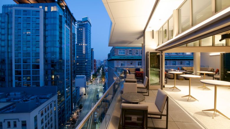 The image features a modern balcony with sleek furniture, overlooking a city skyline at dusk, highlighting urban life.